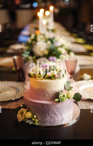 Torta nuziale bianca decorata con fiori su un tavolo servito. Sfondo nero di un ristorante. Festa serale, festa. Foto Stock