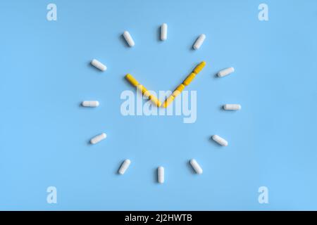 Orologio fatto di pillole bianche e gialle su sfondo blu Foto Stock