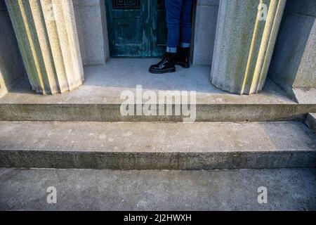 Una persona si erge da sola dalle porte di un mausoleo con pilastri Foto Stock
