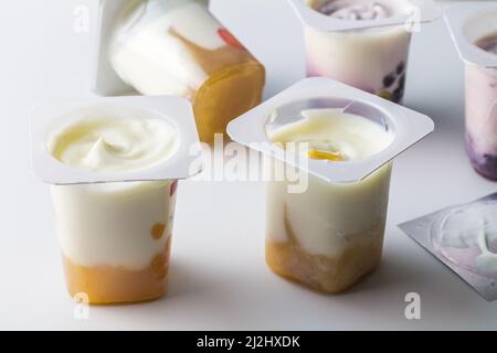 Yogurt aromatizzato alla frutta in tazze trasparenti di plastica su sfondo bianco con coperchio in lamina d'argento - sfondo in tazza di yogurt con fuoco selettivo Foto Stock