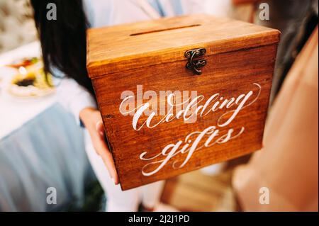 Regali di nozze. La bridesmaid tiene una scatola di legno con un segno manoscritto. Presentare la scatola per il matrimonio. Foto Stock