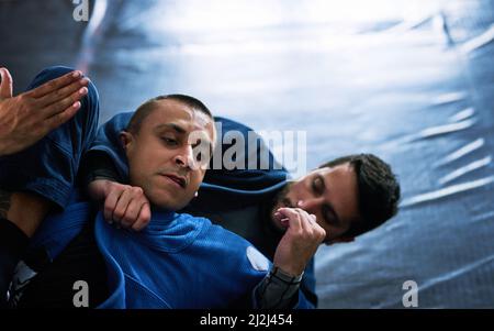 Toccare verso l'esterno. Scatto corto di due giovani atleti maschi che sparano sul pavimento del loro dojo. Foto Stock
