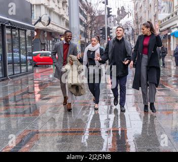 Quattro busiensi multirazziali stanno camminando sulla pioggia insieme mentre parlano del commercio Foto Stock