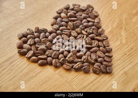 Primo piano di chicchi di caffè a forma di cuore, cuore di valentine di caffè, chicchi di caffè. Isolato su sfondo di legno Foto Stock