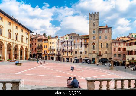 Coppia seduta a terra nella famosa Piazza Grande nel centro storico di Arezzo Foto Stock