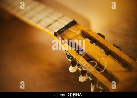 Il collo di una bella chitarra d'epoca con corde metalliche, che si trova su un tavolo di legno in una giornata di sole. Arte e musica. Solfeggio. Foto Stock