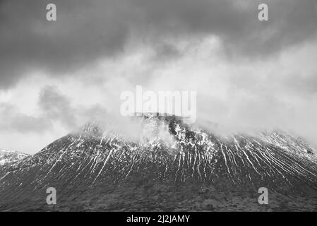 Bianco e nero bellissima immagine di paesaggio invernale di Beinn A’ Chaladair in Scozia con cieli spettacolari Foto Stock