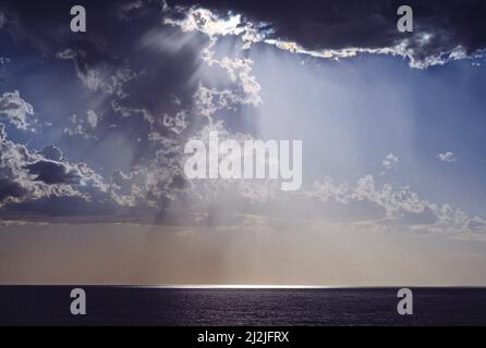 La luce del sole splende attraverso il cielo tempestoso sull'oceano. Foto Stock