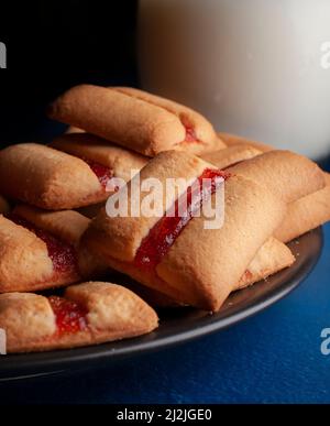 Una pila di biscotti strawberry bar con un bicchiere di latte freddo e fragole fresche naturali sul cibo scuro laterale Foto Stock