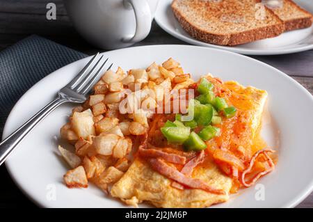 Omelette con formaggio, pomodoro rosso e salsa piccante di cipolla e cubetti di peperoni verdi sopra con un lato di patate fritte quadrate Foto Stock