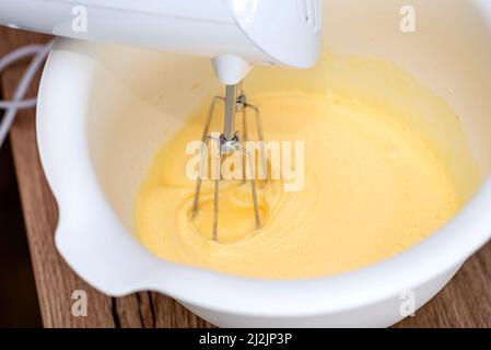 Impastando l'impasto con un mescolatore a mano con una frusta, l'impasto è allo stato liquido giallo. Foto Stock