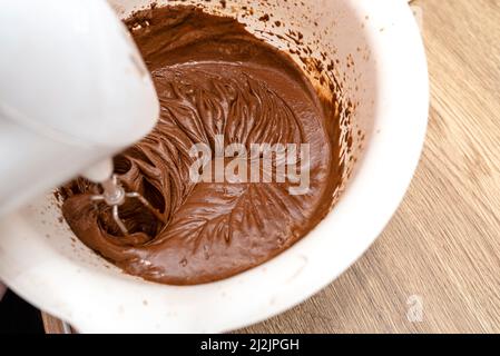 Mescolando l'impasto con un mescolatore a mano con una frusta e burro fuso aggiunto, l'impasto è in una massa liquida spessa marrone. Foto Stock