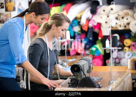 Tutto deve essere perfetto. Due donne che lavorano su un abito in un banco da lavoro all'interno del loro negozio di tessuti. Foto Stock