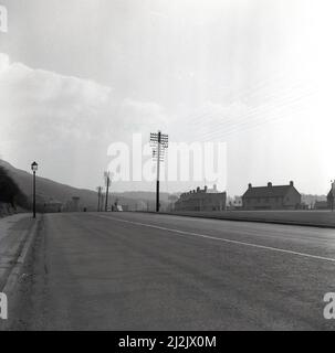 1950s, strada storica e vuota nelle valli della regione industriale di South Wale con area periferica dell'Abbey Works, il gigantesco stabilimento siderurgico di Port Talbot, Galles, Regno Unito, a destra della foto, Foto Stock