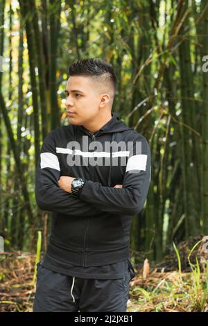 giovane latino arrabbiato per deforestazione, nel mezzo di una bella foresta di bambù nelle maestose montagne colombiane, in posa con le braccia incrociate. Foto Stock