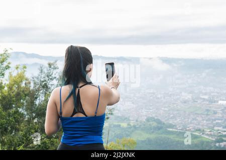 ragazza influencer creazione di contenuti per i suoi social network, durante l'escursionismo. concetto di tecnologia. latina donna escursioni in una giornata fredda per scattare foto di t Foto Stock