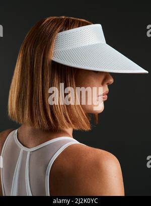 Vi consiglio di indossare la visiera. Scatto corto di una giovane donna sportiva che indossa una visiera parasole su sfondo scuro. Foto Stock