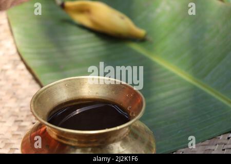 Un vaso di ottone riempito di acqua e foglia di banana con banana sullo sfondo come qualche pratica tradizionale sta facendo Foto Stock