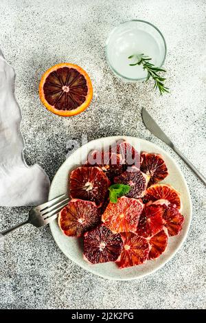 Vista dall'alto di un piatto di arance siciliane sbucciate e affettate con un bicchiere d'acqua rosmarino Foto Stock