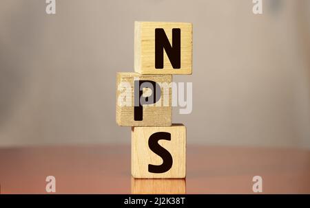 Primo piano la mano del giovane uomo in un cubo di blocco di legno della camicia bianca per la scritta NPS sul pavimento del tavolo di marmo bianco. Foto Stock