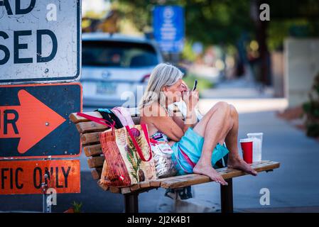 Vecchia donna senza tetto che cazzo sopracciglia su una panchina centro di Scottsdale, Arizona, Stati Uniti. Foto Stock