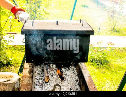 Smokehouse per fumare caldo sul fuoco. Un uomo versa l'acqua nella serranda di una casa di fumo. Foto Stock