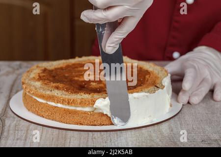 Confettatrice in borgogna kittel decora la torta con la panna Foto Stock