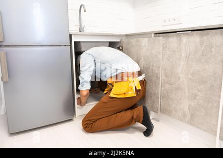 Il padrone nella forma fa l'installazione o lo smontaggio di un tubo dell'acqua o installa un miscelatore nella cucina Foto Stock