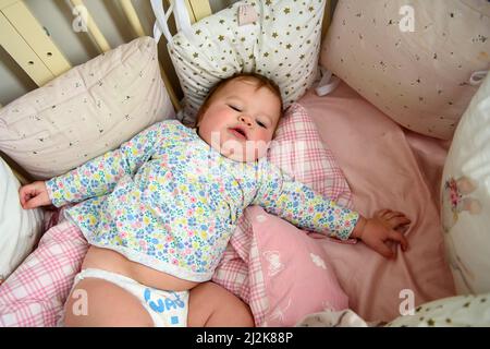 Ragazza carina di dieci mesi, giocando da sola in una culla a casa nel pomeriggio o al mattino Foto Stock