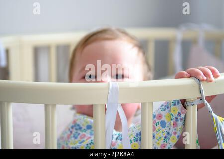 Ragazza carina di dieci mesi, giocando da sola in una culla a casa nel pomeriggio o al mattino Foto Stock