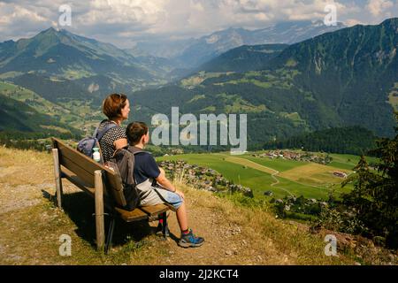 Madre e figlio seduti su una panchina godendo di una vista incredibile in alto nelle Alpi Vaud mentre si escursioni in una giornata di sole in estate. Leysin, Svizzera Foto Stock