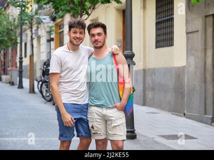 Coppia gay sorridendo abbracciando e guardando la macchina fotografica in strada. Foto Stock