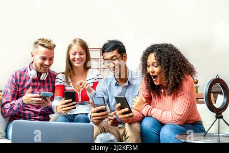 gruppo di creatori di contenuti giovani che guardano gli smartphone il loro successo on line, quattro blogger persone che lavorano in studio per le imprese, giovani lavoro di squadra Foto Stock