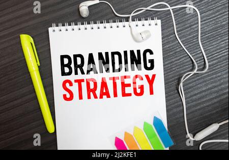 La scrittura di un testo che illustra la strategia di marca. Il concetto di business per l'idea di Marketing Plan scritto su una nota adesiva carta, legno marcatore di sfondo giallo piegato pap Foto Stock