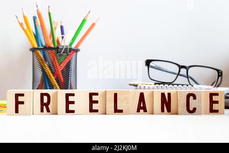 Parola FREELANCE su cubi di legno su sfondo bianco lucido. Foto Stock
