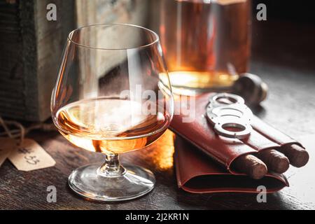 Whisky invecchiato e sigaro in vecchio magazzino distilleria. Sigaro e bicchiere di whisky con ghiaccio in una vecchia distilleria. Foto Stock