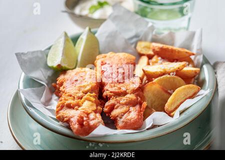 Pesce arrosto e patatine servite con lime e sale. Pesce classico e patatine servite in carta. Foto Stock