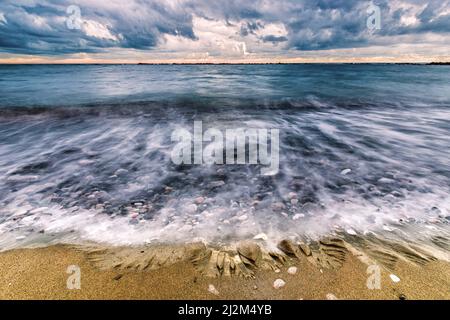 Un bel colpo di onde che si infrangono su una spiaggia sabbiosa sotto un cielo nuvoloso a Viareggio, Italia Foto Stock