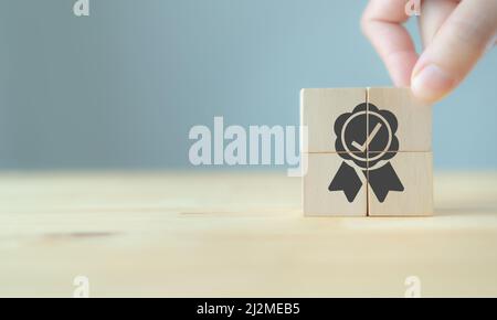 Concetto di garanzia di qualità. La mano dell'uomo mette i cubetti di legno con l'icona di garanzia di qualità sui cubetti di legno con sfondo grigio. Utilizzato per banner e annunci pubblicitari Foto Stock