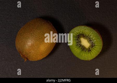 Frutta Kiwi su sfondo nero. Kiwi intero e tagliato a metà. Vista dall'alto con spazio di copia, disposizione piatta. Foto Stock