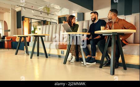 Team di uomini d'affari che lavorano in una lobby d'ufficio. Tre uomini d'affari felici sorridendo mentre hanno una discussione. Gruppo di imprenditori moderni collabora Foto Stock