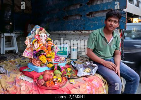 Durante il festival Ganesh Chaturthi a Mumbai, India, un giovane uomo indiano si siede in un camion aperto accanto ad una figura colorata di Dio elefante (indù) Ganesh Foto Stock