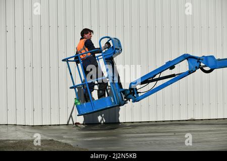 Un costruttore usa un selezionatore di ciliegia per accedere alle aree difficili mentre galleggia da una lastra di calcestruzzo appena versata Foto Stock