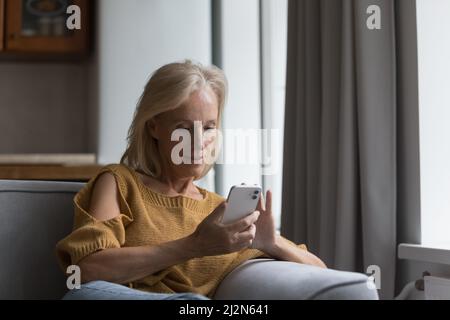 Donna bionda matura focalizzata che legge il messaggio di testo sullo smartphone Foto Stock