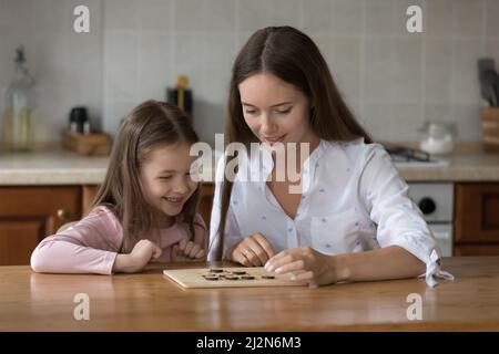 Mamma felice e figlia ragazza impegnata in gioco da tavolo di apprendimento Foto Stock