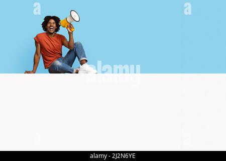 Un uomo afro-americano positivo seduto su un tavolo vuoto, facendo annuncio Foto Stock