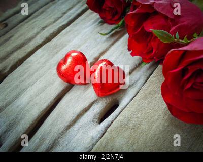 Rose rosse e due cuori di cioccolato per San Valentino su sfondo tavola di legno. Foto Stock