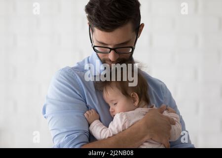 Papà giovane e tranquillo in occhiali che tengono sonnolenta figlia del bambino Foto Stock