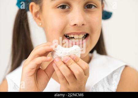 L'adolescente sta tenendo un modello del getto dentale all'inizio del trattamento ortodontico accanto ai suoi denti dopo che il trattamento è stato completato. Foto Stock