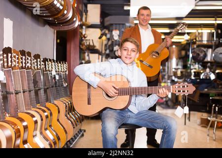 Il venditore allegro mostra la chitarra al cliente ragazzo Foto Stock